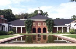 A red brick building and three sides of a white columned cloister behind a large reflecting pool