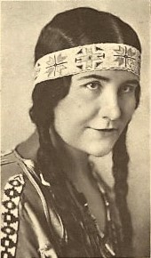 Photograph of a Native American woman with long braids wearing a buckskin dress and adorned with a beaded headband and bead necklace.