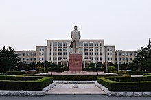 A photo of the Dalian University of Technology. A large statue of a famous Chinese person stands in the square of a sprawling university complex.