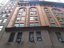 Windows on South Beaver Street. The lower part of the facade is made of dark brownstone with narrow rectangular windows. The upper stories of the facade contain several sets of windows within four-story-tall arches made of orange and brown brick