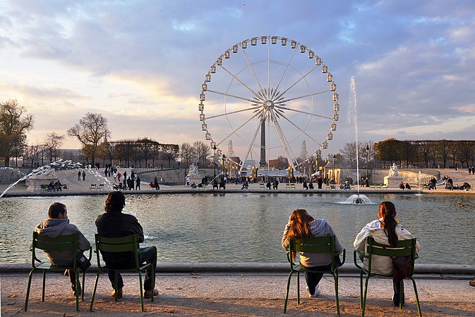 圖為在巴黎摩天輪（法國）前的杜樂麗花園坐著的人們，這座60公尺高的摩天輪最初是為了慶祝千禧年活動而設立的。