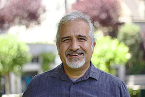 Photo of a man with a nice smile, a blue shirt, and a white beard