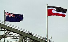 The black, white and red Tino Rangatiratanga flag and New Zealand national flag flying above a bridge