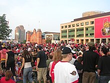 Large crowd of people in front of building decorated with Ottawa Senators logo