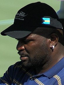 A man in a blue shirt with gray, white, and black stripes, wearing a black baseball cap.