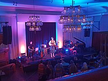 View from the balcony of three musicians on a small stage in a small auditorium