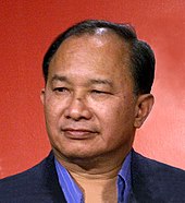 A photo of a Chinese man wearing a black suit against an orange backdrop.