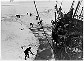 Men with digging tools removing ice surrounding the ships hull, creating an icy pool of water