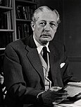 Harold Macmillan, wearing a jacket and tie, sitting at a desk