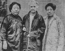 Three women standing side by side; Ida Kahn is a middle-aged Chinese woman wearing a silk tunic; Gertrude Howe is an older white woman wearing a silk jacket; Li Bi Cu is a middle-aged Chinese woman wearing a light-colored jacket