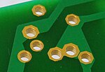 Close-up view of a printed circuit board showing component lead holes (gold-plated) with through-hole plating (Through-hole technology).