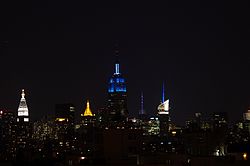 Upper floors of the Empire State Building lit in blue, amid other lit skyscrapers