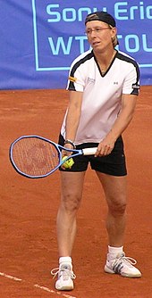 A woman, with a white shirt and black shorts is standing up