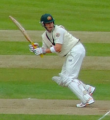 A man in cricket whites and baggy green walking towards the camera