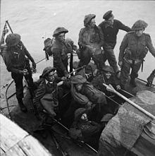 nine British soldiers and one sailor on a small boat at sea. A union Jack flies from a mast at the rear