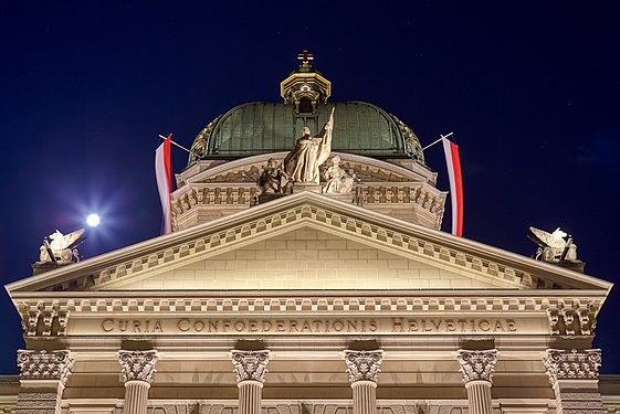 Federal Palace of Switzerland with full flags due to Indian President's state visit. Plaza view during full moon with clear night sky.