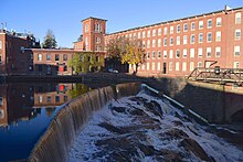 A red brick building built over a waterfall. The waterfall is a concrete dam structure.