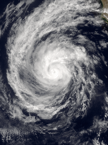 A photograph of a hurricane off the Pacific coast of Mexico; the eye is obscured by clouds, and a long, wide spiral band of clouds begins on the northern flank before curving all the way around the hurricane