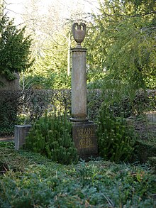 Grave with a golden inscription on the base of a round marble pillar surmounted by an urn