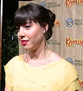 A dark brunette woman wearing a yellow dress smiles