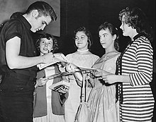 Elvis Presley signing autographs for a group of young female fans.