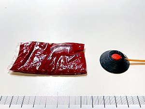 A 15 g packet of fake blood next to a 0.5 grain squib with a solid polycarbonate shield.