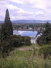 Broad view over a city from an elevated viewpoint, with a reservoir in the near distance