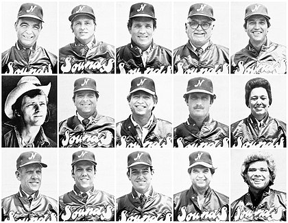 An array of 14 men and 1 woman. Most are wearing satin jackets with "Sounds" across the front and baseball caps with an "N" in the center. One man is wearing a denim jacket and cowboy hat.