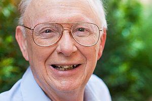 A smiling man with white hair wearing bifocals.