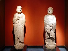 Two monks, one holding hands in front of chest, the other hands folded in front of belly
