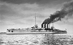 大型灰色战列舰于海上。黑烟从其三个紧密排列的烟囱中飘出。
