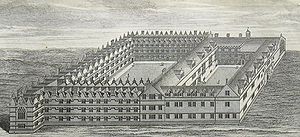 A bird's-eye view of two joined quadrangles of buildings, the left quadrangle being slightly larger than the right; the buildings on the far left extend beyond the adjoining range slightly, terminating in a large Gothic window; regularly positioned smaller windows and gables throughout both quadrangles