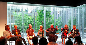 Mekons seated on a stage with a crowd