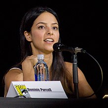 Tala Ashe sitting down behind a name plate reading Dominic Purcell and a microphone