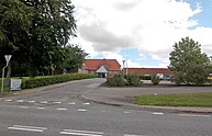 A paved road leads to a driveway where a small building is seen