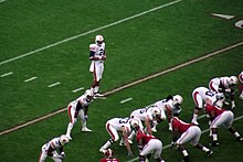 A quarterback is behind the offensive line preparing to take a snap.