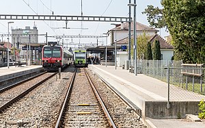 Red and green trains on a double-tracked railway line surrounded by platforms