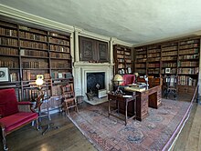 A domestic library with wood-panelled walls, a large wooden deck and an antique fireplace