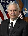 man in business suit, American flag and Department of Defense flag in background