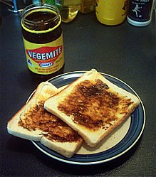 Slices of pale bread covered with a thick, dark brown spread; a jar filled with the spread is labelled: Vegemite