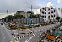 A road junction adjacent to the construction site in the foreground, with cranes and construction machinery