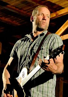 middle-aged white male playing guitar onstage, looking left of camera