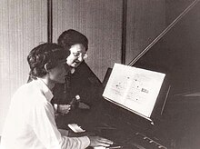 Piano teacher sitting left of a student at a great piano