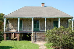 A cottage with natural walls and a large front porch on a tall brick foundation.