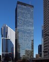 Ground-level view of a black, rectangular high-rise. its glass facades are highly reflective and the smaller facade is bisected by black, inset, crisscrossed beams