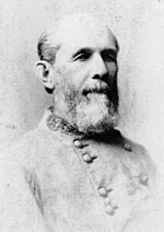 Black and white photo shows a bearded, balding man in a double-breasted gray military uniform.