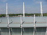 view from above of the roof of a curved roof of a building with tall white poles and various cables connecting them