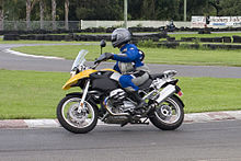 Black and yellow BMW R1200GS motorcycle, being ridden around a corner on a race track by a rider in a blue and grey suit