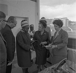 A black and white photo of the subject looking down, surrounded by others.