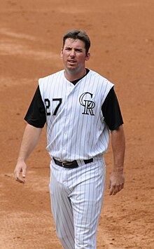 A man in a white baseball uniform with black sleeves